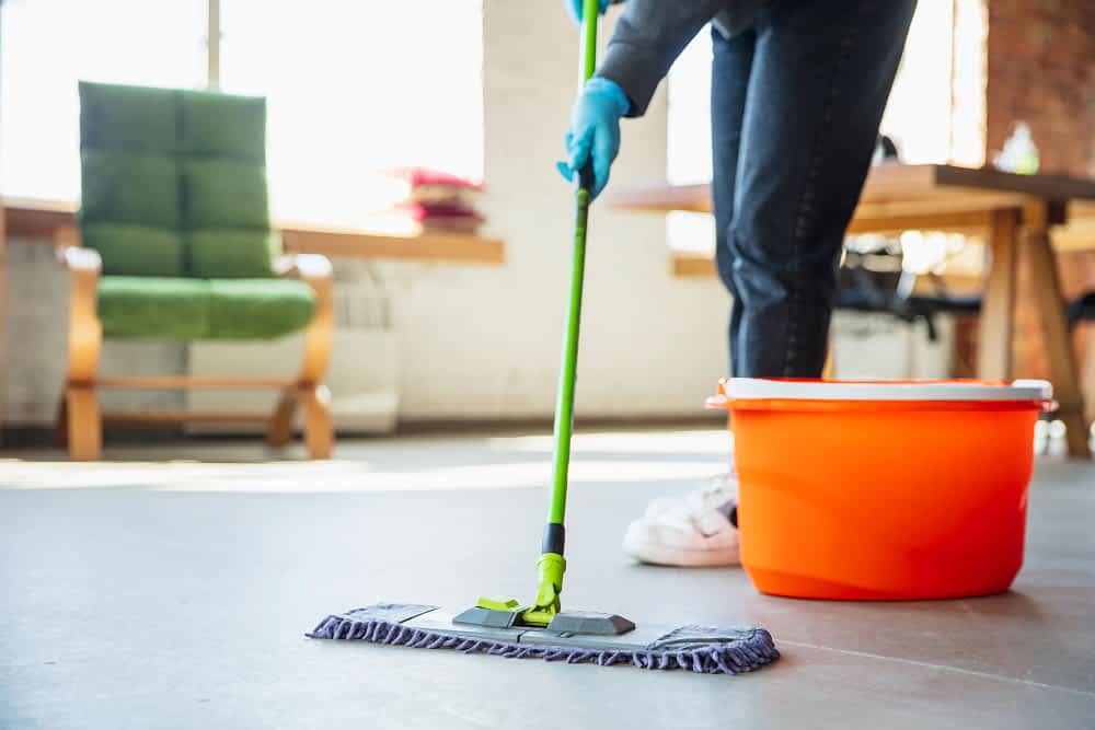 A professional house cleaner uses a green mop and orange bucket to clean the floor of a condo or loft.