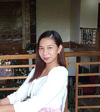 A formally dressed woman in white sitting down at a restaurant looking into the camera
