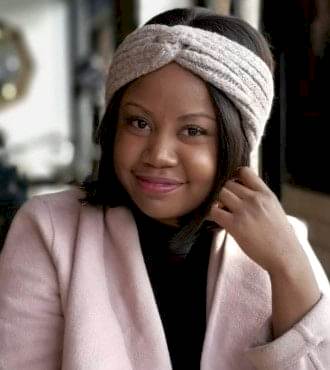 A woman in a light pink blazer looking into the camera smiling